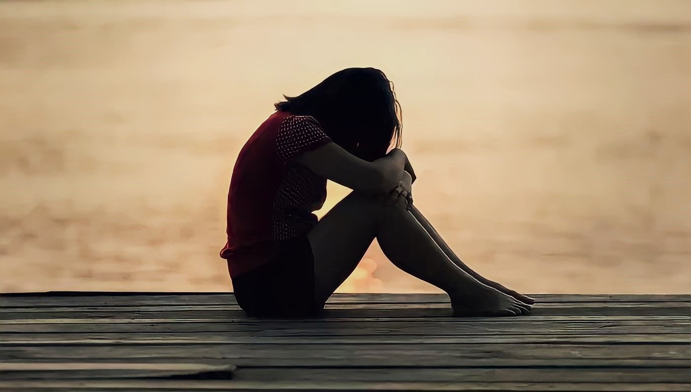 Mulher sentada com cabeça encostada nos joelhos